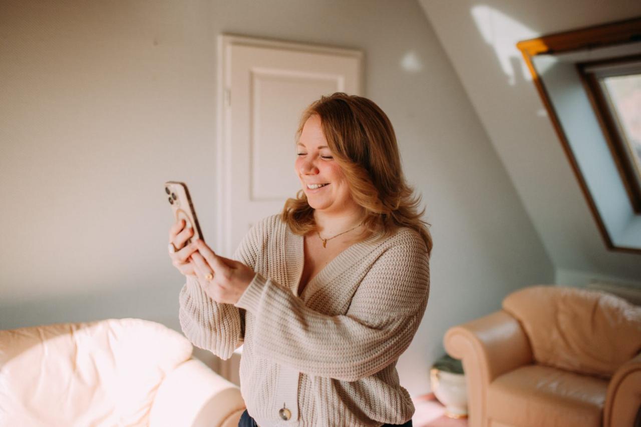 Janine lächelnd mit dem Handy im sonnigen Raum